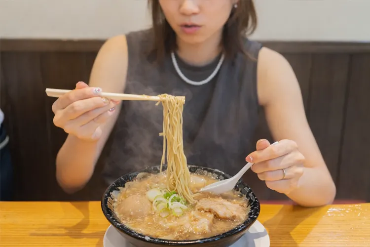 女性が背脂ラーメンを箸で持ち上げて食べている様子