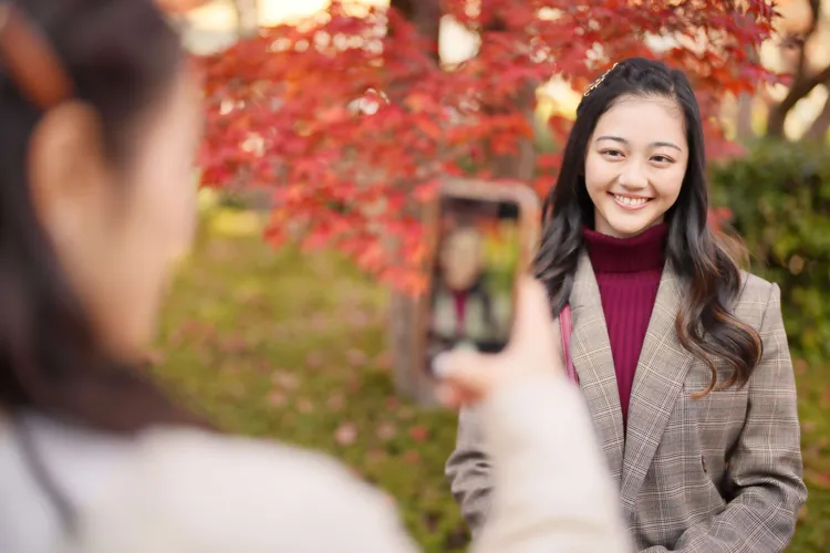 紅葉をバックに写真を撮る女性