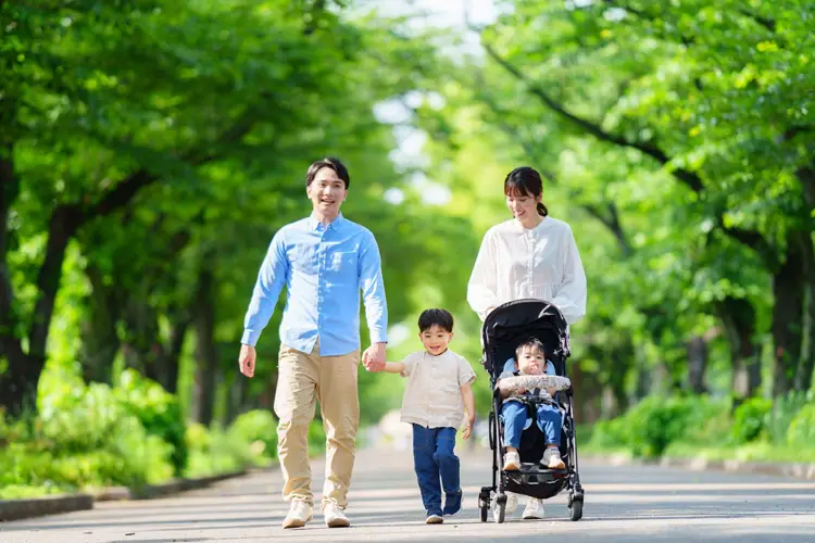 緑の街路樹を歩くベビカーを押した4人家族